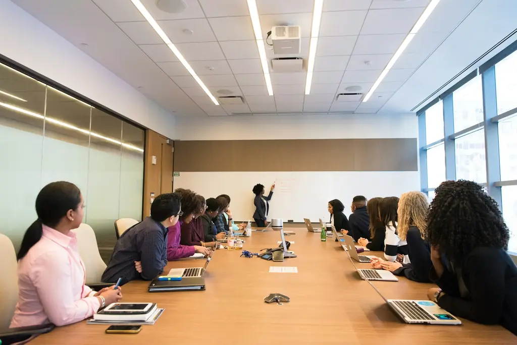 Team around a boardroom table listening to a colleague presenting at a whiteboard