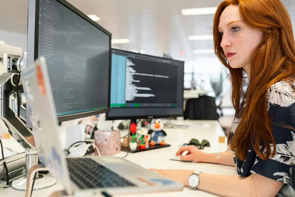 Analyst concentrating on multiple monitors at her desk in an office