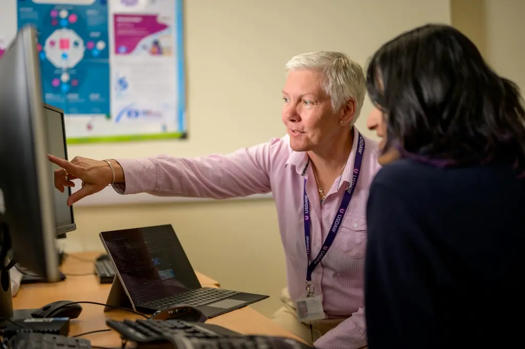 IT support colleague pointing at a computer screen while helping a co-worker at her desk