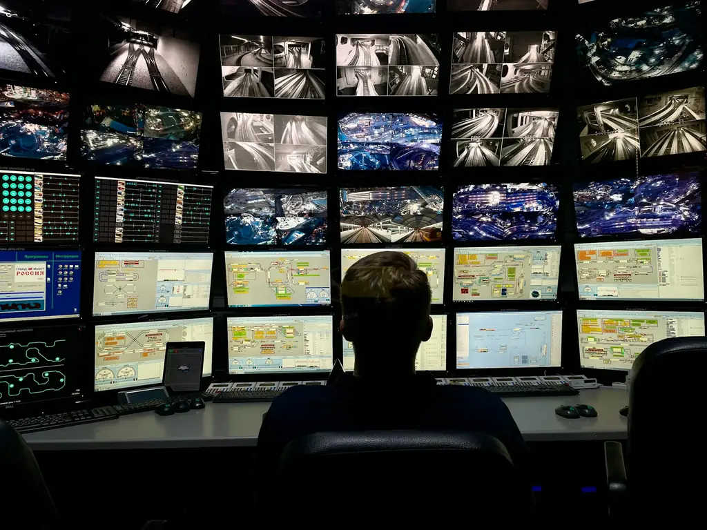 Operator seated in front of a large wall of monitoring screens