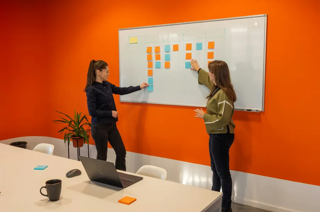 Two colleagues planning a project with sticky notes on a meeting-room whiteboard